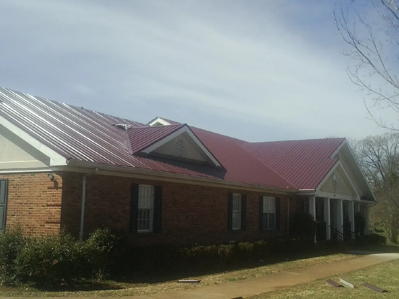 Red metal roof with gabled entries on a long brick building, from a Hail Damage Roof Repair job in Placerville
